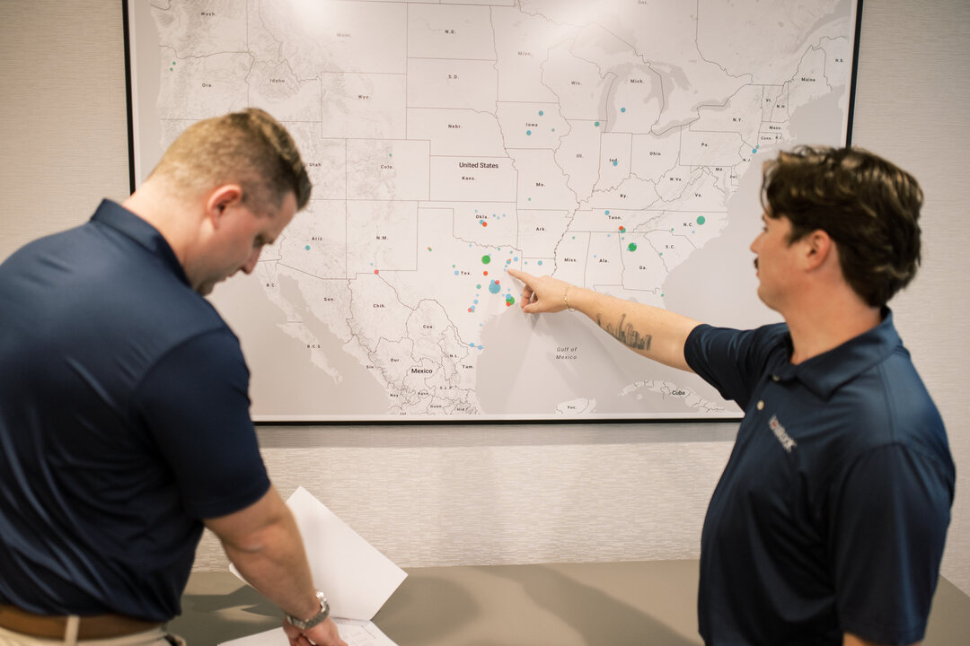 two men point at Dallas on map of USA